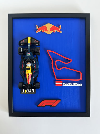 Framed display of a Formula 1 car model and Red Bull Ring track layout with Red Bull logo on a blue background.